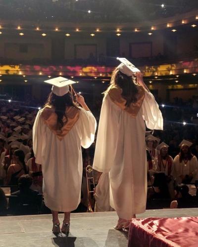 image of 2 girls in cap and gown standing on stage looking out to audience